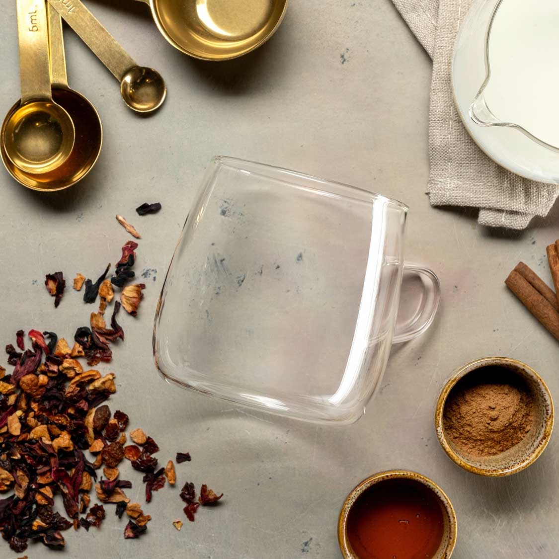 Teetasse mit Tee-Zubehör und Trockenblüten auf grauem Untergrund arrangiert