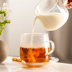 Teetasse wird mit heißem Wasser gefüllt, daneben Tee und Blumen