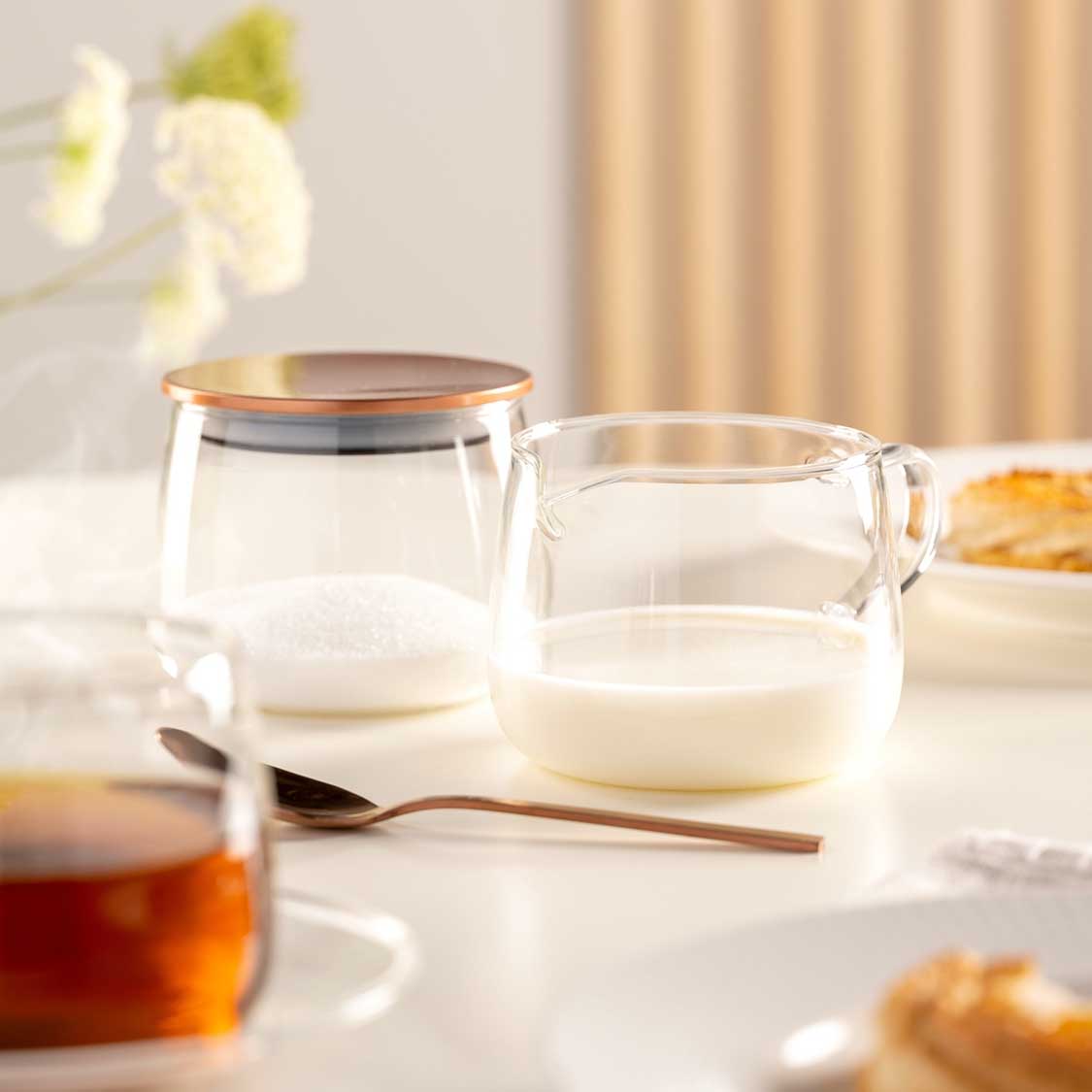 Milchkännchen TÈ PER TE auf gedecktem Tisch mit Tasse und Gebäck