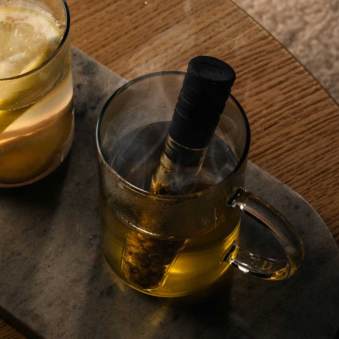 Teeinfuser TÈ PER TE in Borosilikat-Glaskanne mit Tee, daneben gefülltes Glas auf Holztisch