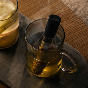 Teeinfuser TÈ PER TE in Borosilikat-Glaskanne mit Tee, daneben gefülltes Glas auf Holztisch