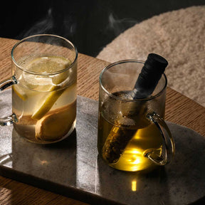 Zwei Teeinfuser TÈ PER TE in Glastassen mit heißem Wasser auf Marmortisch