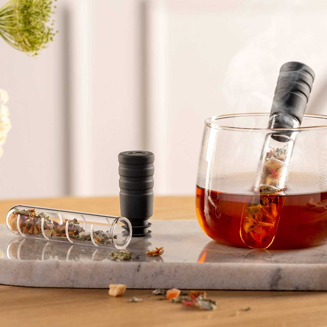 Teeinfuser neben Teeglas mit Tee auf Marmortablett, Teeblätter sichtbar