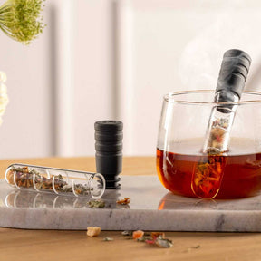 Teeinfuser neben Teeglas mit Tee auf Marmortablett, Teeblätter sichtbar