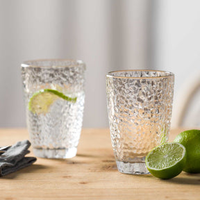 Trinkglas MATERA mit Limettenscheibe auf Holztisch, daneben Limettenhälften