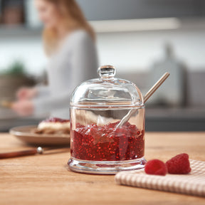 Geleedose DELIGHT mit Himbeeren und Löffel auf Holztisch, Küche im Hintergrund