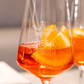 Weißweinglas PUCCINI mit gravierter Krone und orangefarbenem Getränk, daneben weiteres Glas