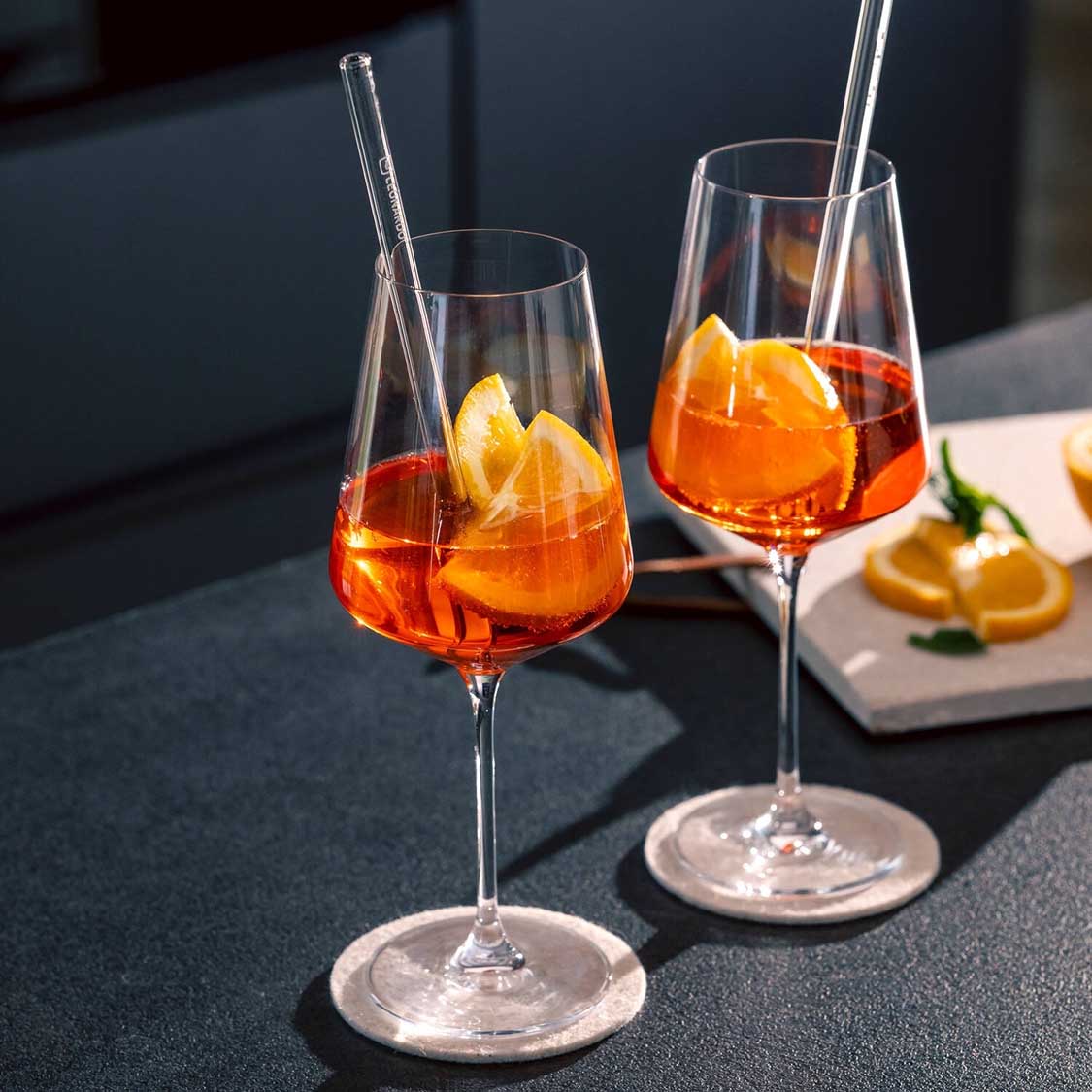 Zwei gefüllte Weißweingläser mit Orangenscheiben und Trinkhalmen auf gedecktem Tisch