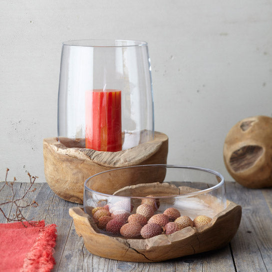 Glasschale mit Teaksockel auf Holztisch, gefüllt mit Nüssen, daneben Kerze in Glas und Deko