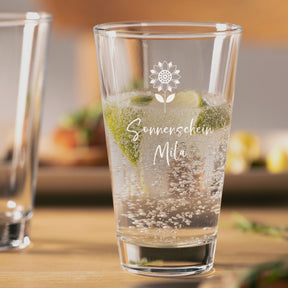 Trinkglas CIAO mit Gravur "Sonnenschein Mila" und Blumenmotiv, gefüllt mit Mineralwasser und Minze, auf Holztisch