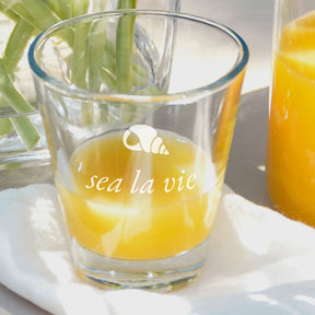 Trinkglas CIAO mit Gravur "sea la vie" gefüllt mit Orangensaft auf weißem Untergrund