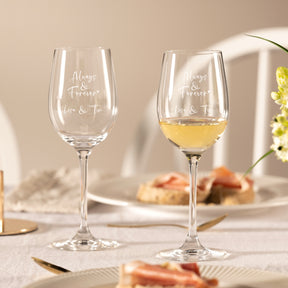 Zwei gravierte Weißweingläser CIAO+ auf gedecktem Tisch, eines leer, eines mit Weißwein gefüllt