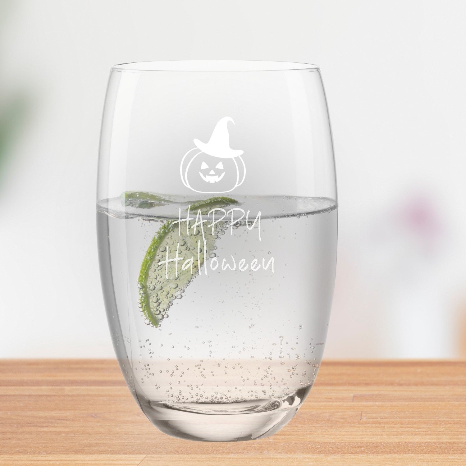 Trinkglas CHEERS mit Halloween-Gravur, gefüllt mit Wasser und Limettenscheibe, auf Holzoberfläche