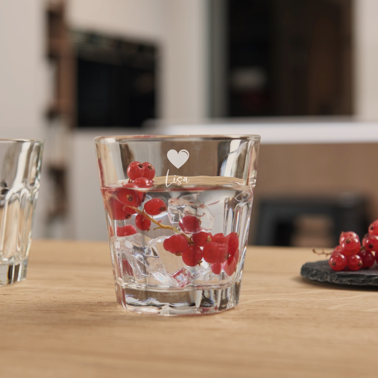 Trinkglas ROCK mit Gravur, gefüllt mit Wasser und roten Johannisbeeren, auf Holztisch