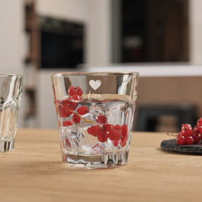 Trinkglas ROCK mit Gravur, gefüllt mit Wasser und roten Johannisbeeren, auf Holztisch