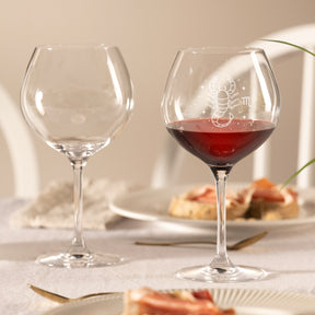 Burgunderglas CIAO+ mit Gravur, eines gefüllt mit Rotwein, auf gedecktem Tisch mit Gebäck