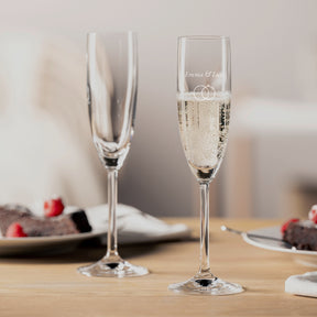 Zwei Sektgläser DAILY mit Gravur auf gedecktem Tisch, eines gefüllt mit Sekt