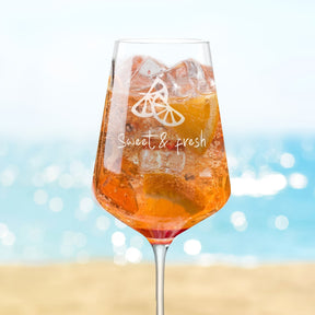 Rotweinglas PUCCINI mit Orangensaft, Eiswürfeln und Zitronenscheiben, Strandszene im Hintergrund