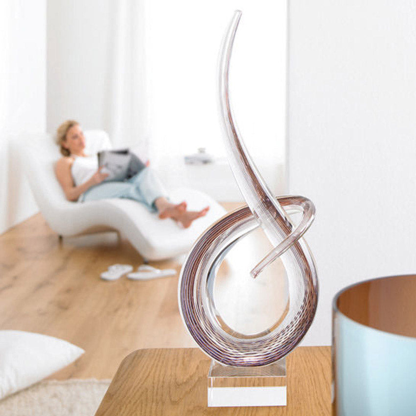 Braune Glasskulptur SCULPTUR 50 cm Ease auf Holztisch, Wohnzimmer mit Person im Hintergrund