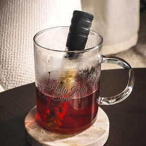 Teeglas NOVO mit rotem Tee und schwarzem Infuser auf Untersetzer, Sticker sichtbar