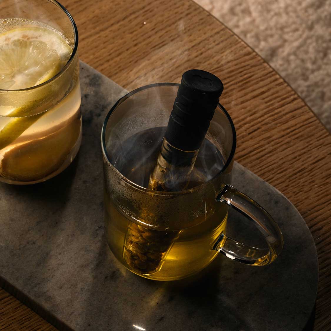 Teeglas NOVO mit Infuser auf Marmortablett, gefüllt mit Tee, daneben Glas mit Getränk