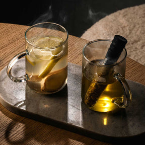 Zwei Teegläser NOVO mit Infuser auf grauem Tablett, gefüllt mit Tee und Zitrone