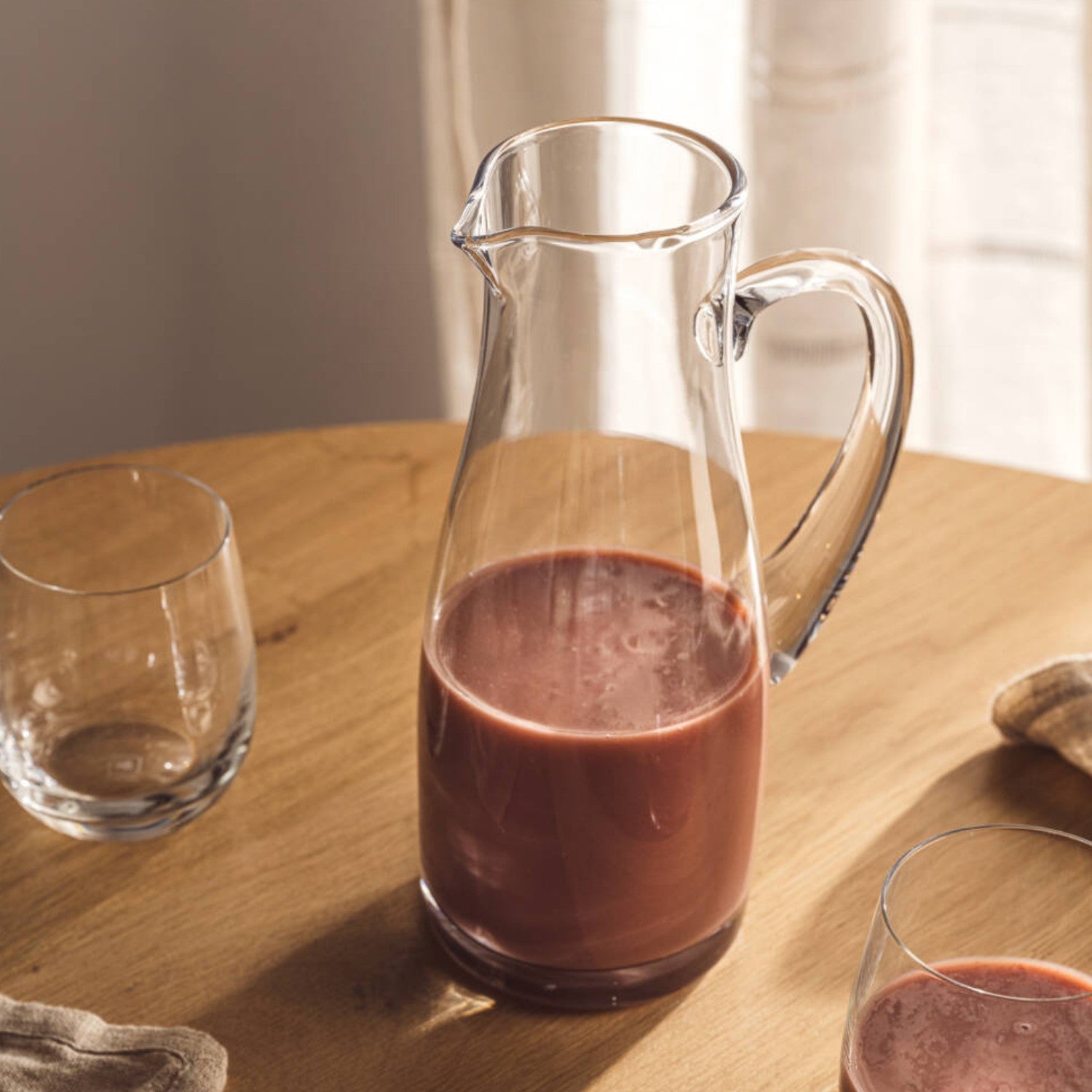 Krug PIENO 1 l mit Rotwein gefüllt auf Holztisch, umgeben von Gläsern