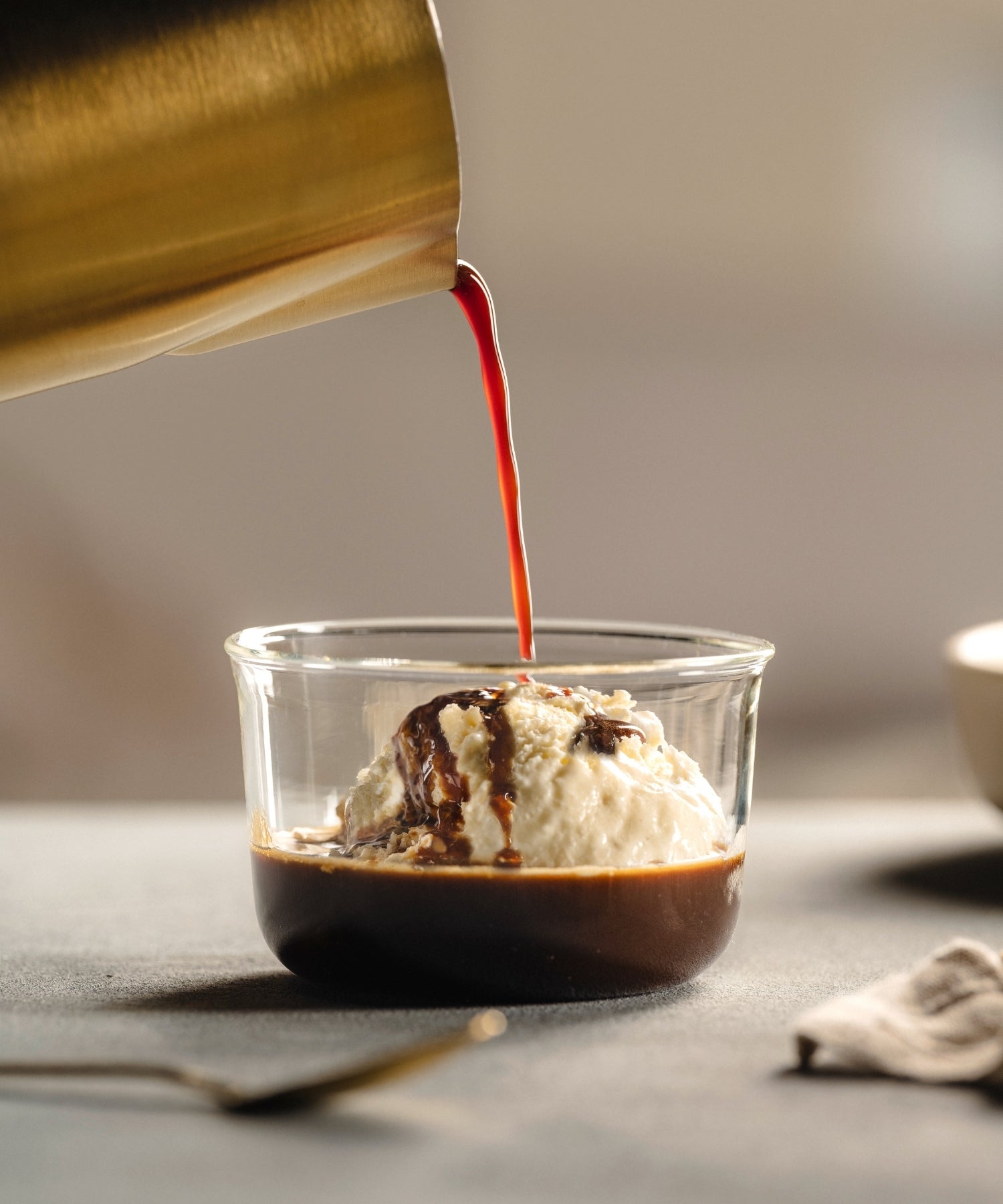 Affogato mit Vanilleeis und Schokolade, heißer Kaffee wird aus goldenem Behälter gegossen, elegante Glasschale, warme Sommeratmosphäre