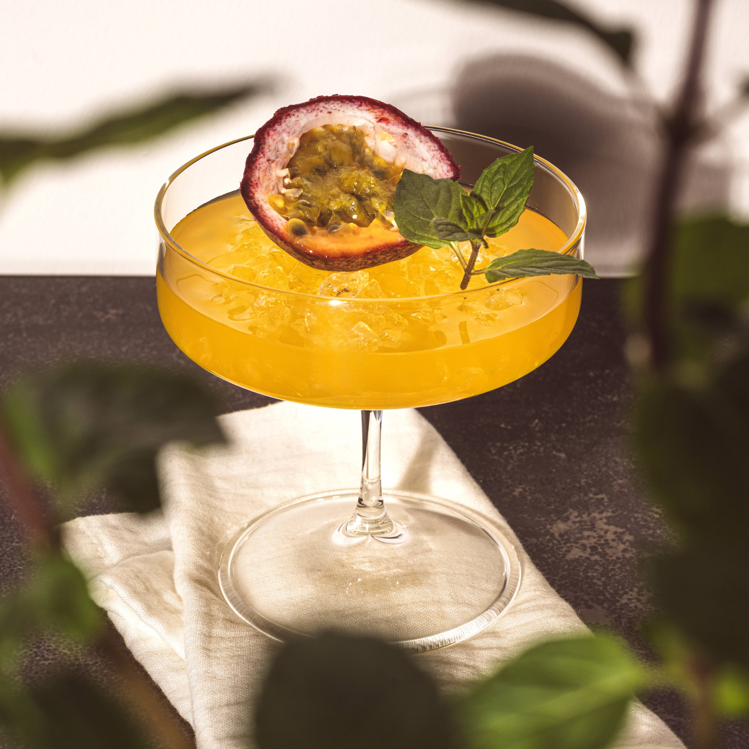Elegantes Cocktailglas BASSO mit gelbem Drink, Passionsfrucht-Scheibe und Minze-Garnierung in Sonnenlicht