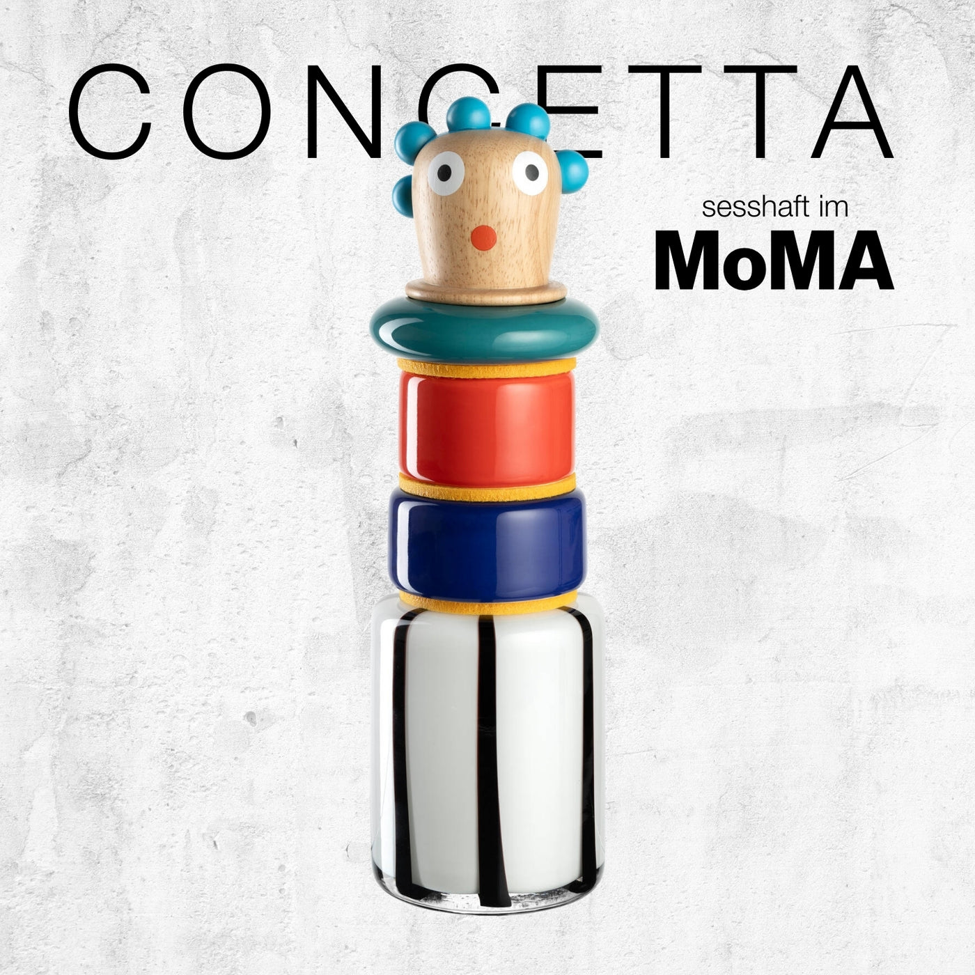 Bunte stapelbare Figur mit blauem Haar, rotem und blauem Mittelteil sowie weiß-schwarz gestreifter Basis. Text: „CONCETTA sesshaft im MoMA“.