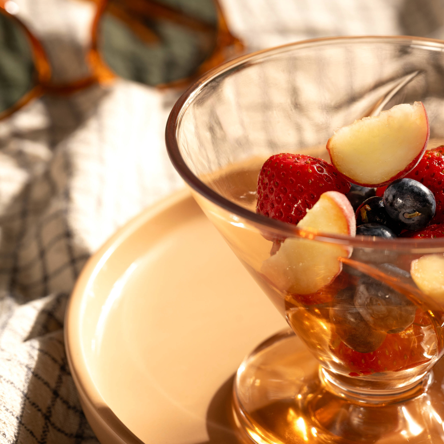Elegante Gläser mit bernsteinfarbenem Getränk, garniert mit frischen Beeren und Apfelscheiben in warmer Sonnenstimmung