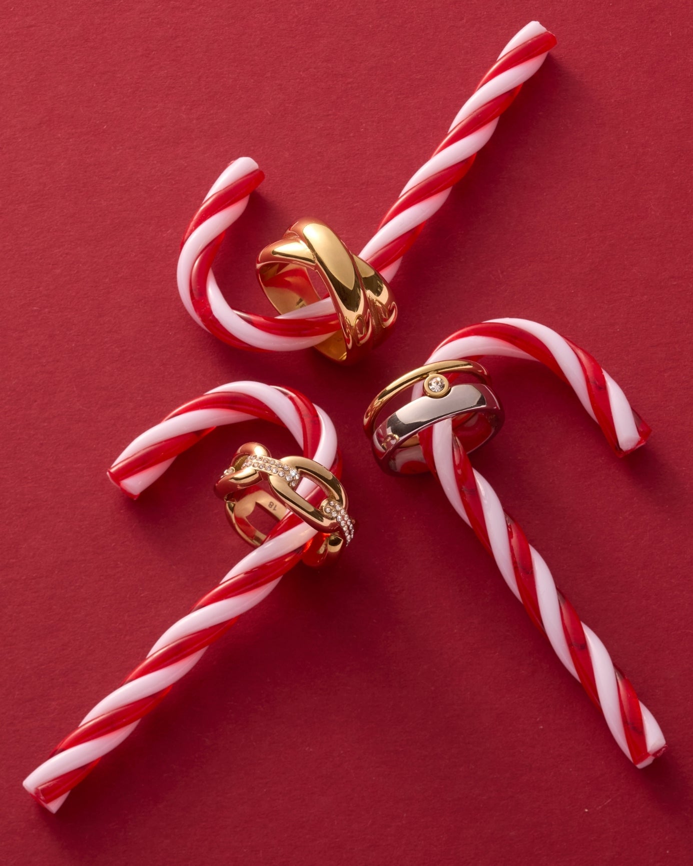 Drei goldene Ringe auf roten und weißen Zuckerstangen vor rotem Hintergrund, festliche Schmuckkollektion