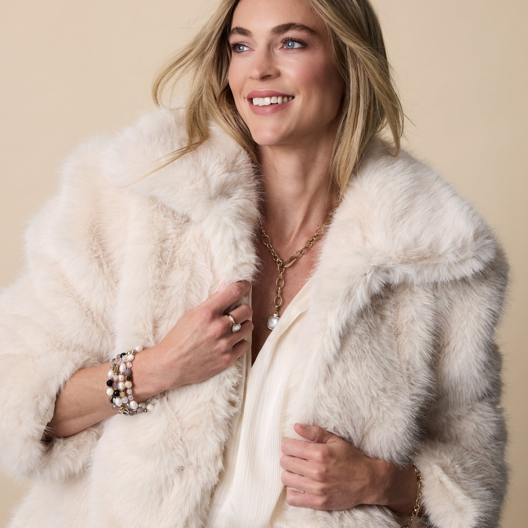 Frau mit blonde Haaren trägt cremefarbenen Cardigan mit Pelzkragen und eleganten Schmuck aus der LEONARDO Jewels by Mauritia Mack Kollektion