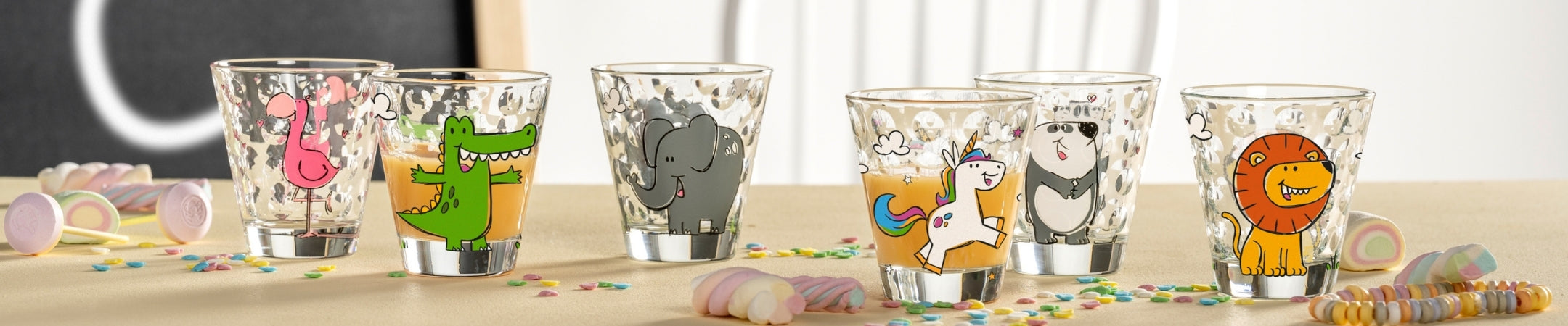 Sechs bunte Trinkgläser mit lustigen Tiermotiven: Flamingo, Dinosaurier, Elefant, Lama, Panda und Löwe auf hellem Untergrund mit Konfetti und Luftschlangen
