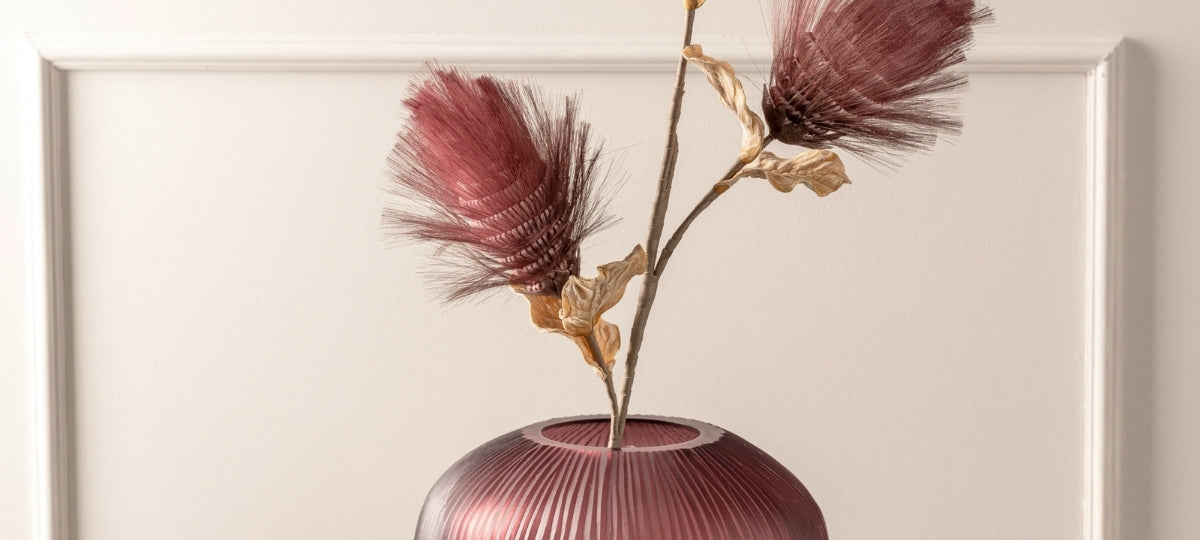 Elegante Dekoblumen mit dunkelroten Blüten in einer glänzenden Vase mit Rillenstruktur vor hellem Hintergrund