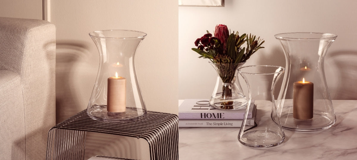Elegante Glasvasen und Windlichter werden minimalistisch mit Blumen und Kerzen auf Möbeln und Büchern arrangiert.