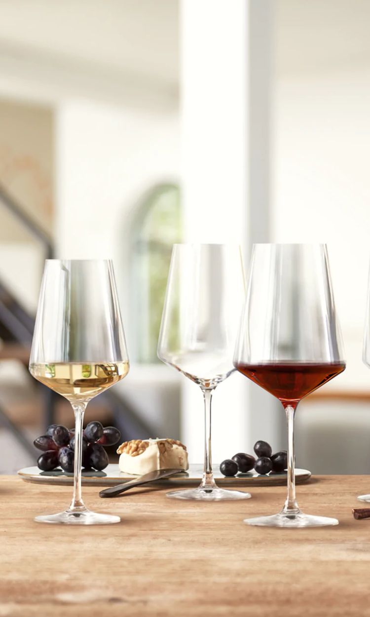 Drei elegante Weingläser auf gedecktem Tisch mit Käse und Trauben