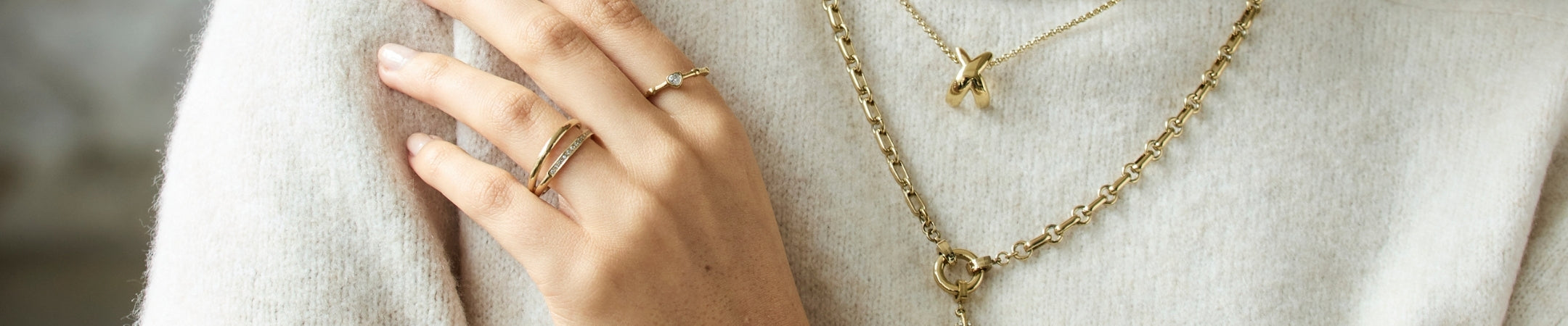 Frau traegt goldene Ketten und Ringe an beiger Kleidung, elegante Schmuckstyles in warmen Metalltönen