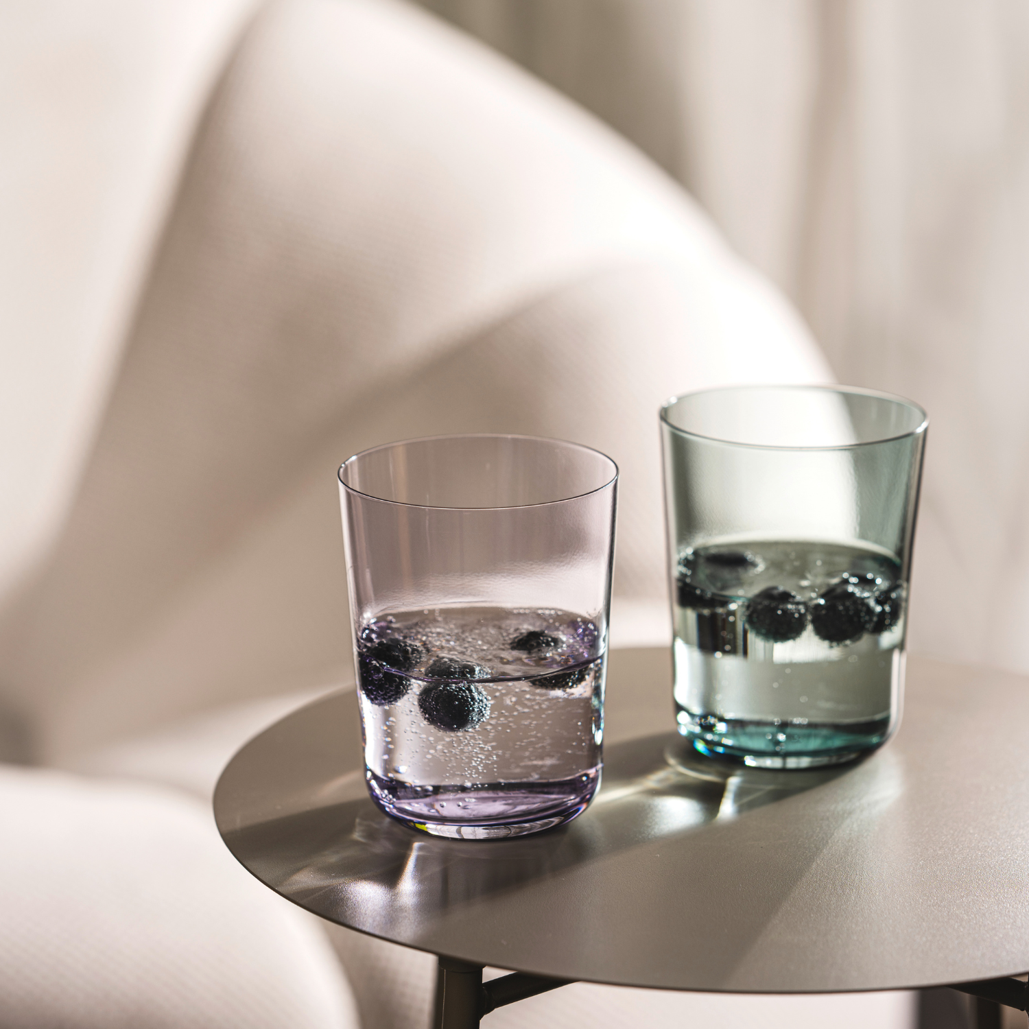 Zwei Trinkgläser mit Getränk und Eiswürfeln auf runder Oberfläche, helles, minimalistisches Setting mit Schattenwurf