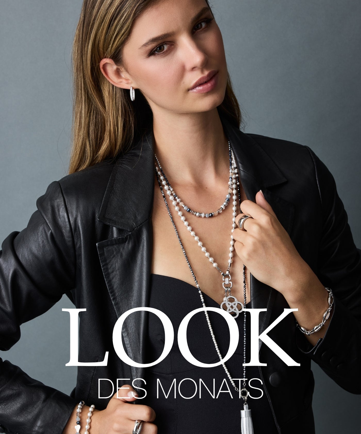 LOOK DES MONATS. Frau in schwarzem Lederblazer mit eleganten Schmucksets aus Perlen und Edelstahl vor grauem Hintergrund