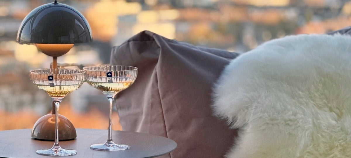 Elegante Cocktailgläser mit Heizstrahler, flauschige weiße Decke, verschwommene Stadtkulisse im warmen Licht