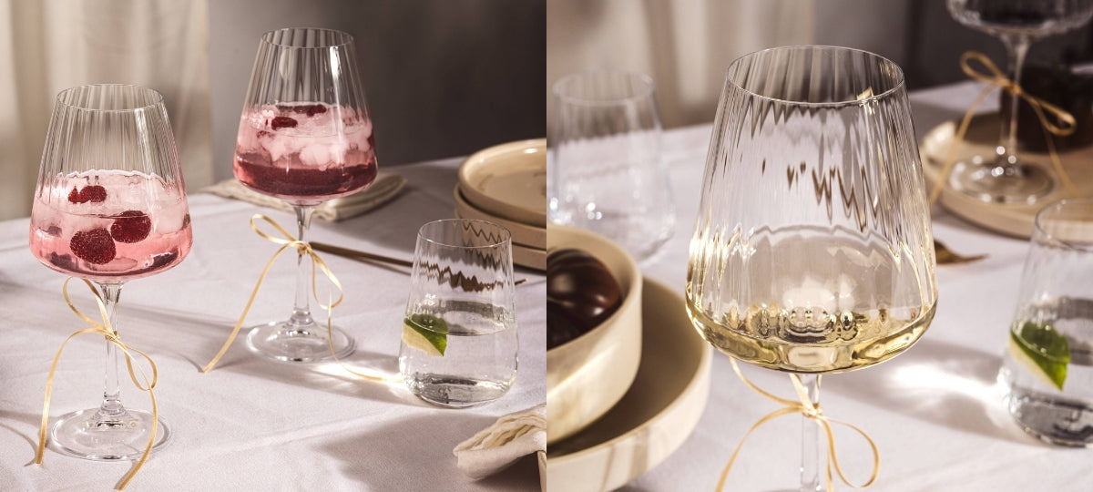 Elegante Gläser mit geripptem Design gefüllt mit rosa und weißem Getränk, golden gebundene Servietten, festlich gedeckter Tisch