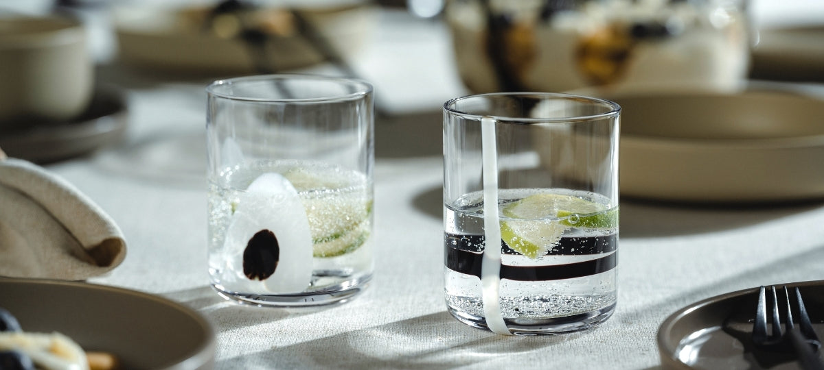 Zwei elegante Gläser mit Mineralwasser und Limette auf weißem Leinen neben Besteck und Tellern