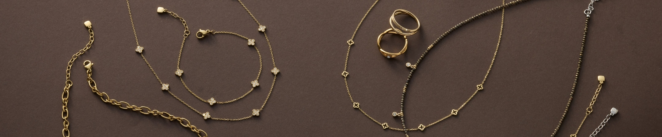 Goldene und silberne Halsketten und Ringe mit Perlen und Steinen auf braunem Hintergrund