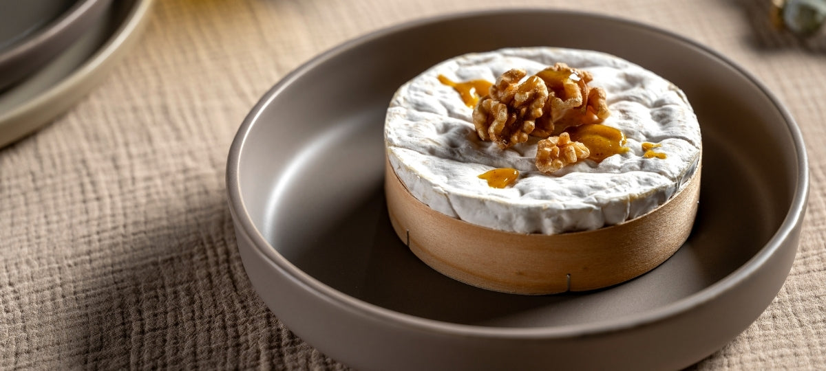 Graue Schale mit Käseplatte, weißem Brie und Walnüssen auf strukturiertem Tischuntergrund