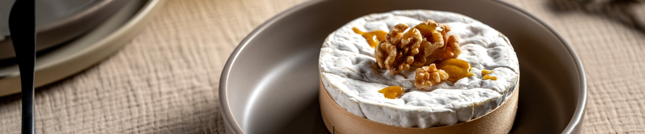Elegante Keramikschale mit Creme-Topping und Nussgarnitur auf grauem Teller, neutrale Tischkulisse