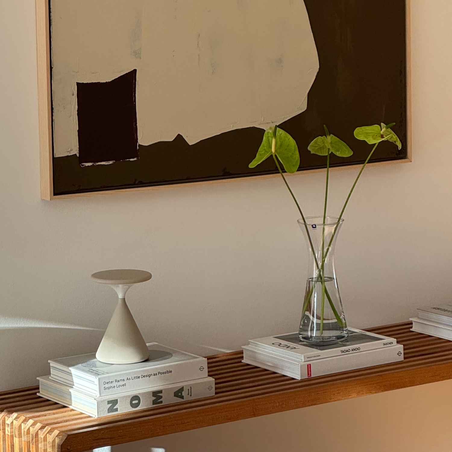 Elegante Glasvase mit frischen grünen Pflanzen auf Holzregal neben Designbüchern und weißem Kerzenständer